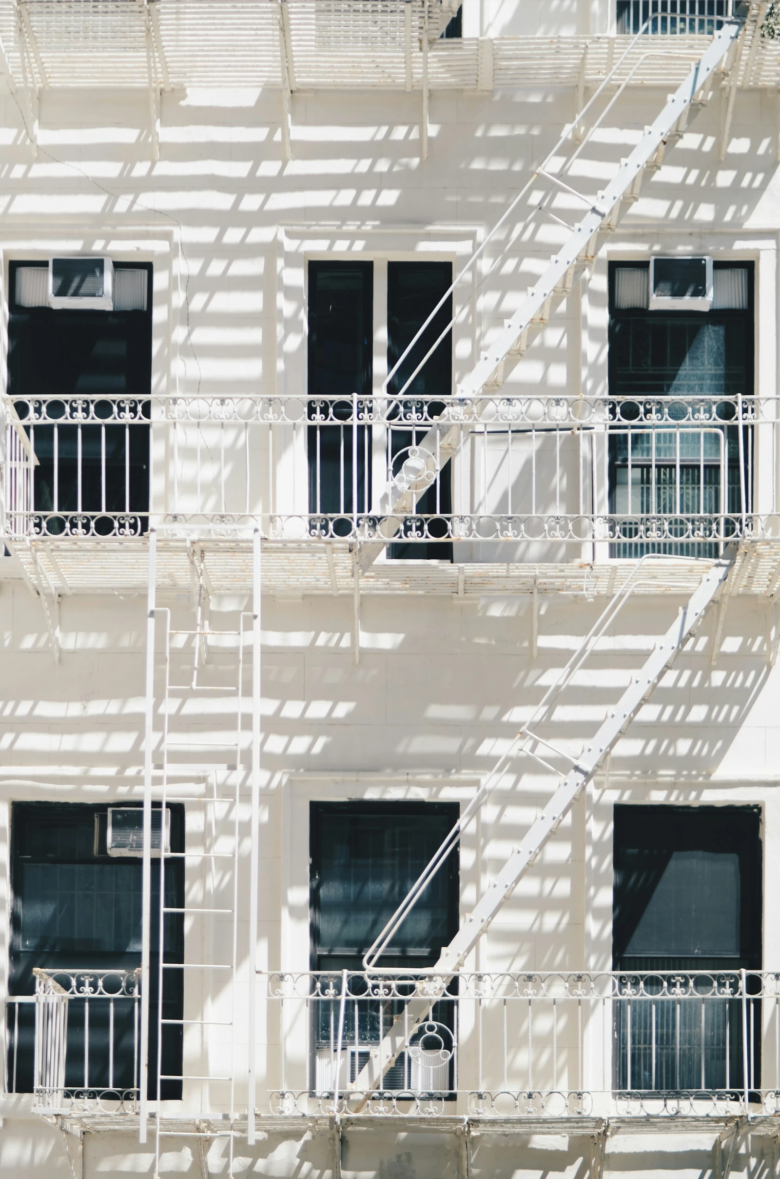 A pale SoHo facade with dark windows and intricate white fire escapes casting geometric shadows in the sunlight.